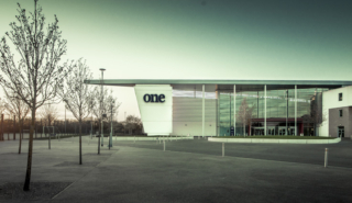 An image of a modern building with a mix of stone and glass on the long wall. set in a landscaped area next to a carpark. Its called Suffolk one. Interior Photographer in London