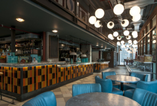 an Interior photograph of Jamie Olivers restuarant in london. there are blue leather seats and big ball lights from the ceiling. a bar is in the background.|David Chatfield Photography