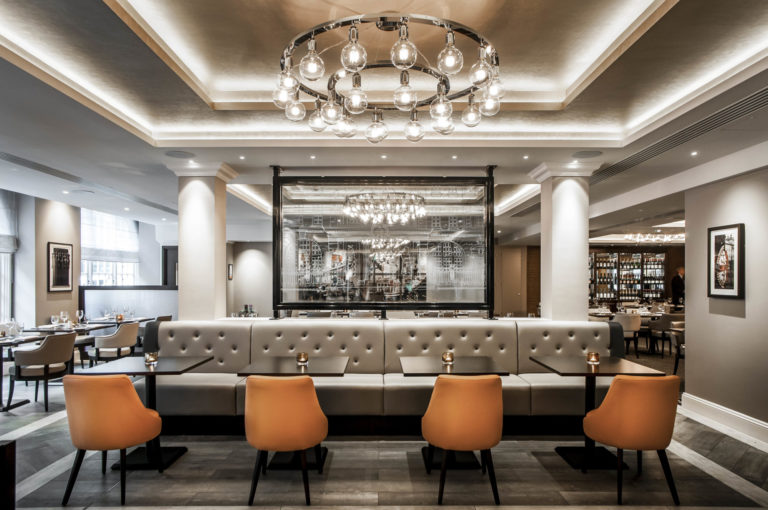 restuarant setting with a leather bench seat and four leather sinle seats warm setting and a big modern chandelier hanging from the ceiling.David Chatfield | Interior Photography in London