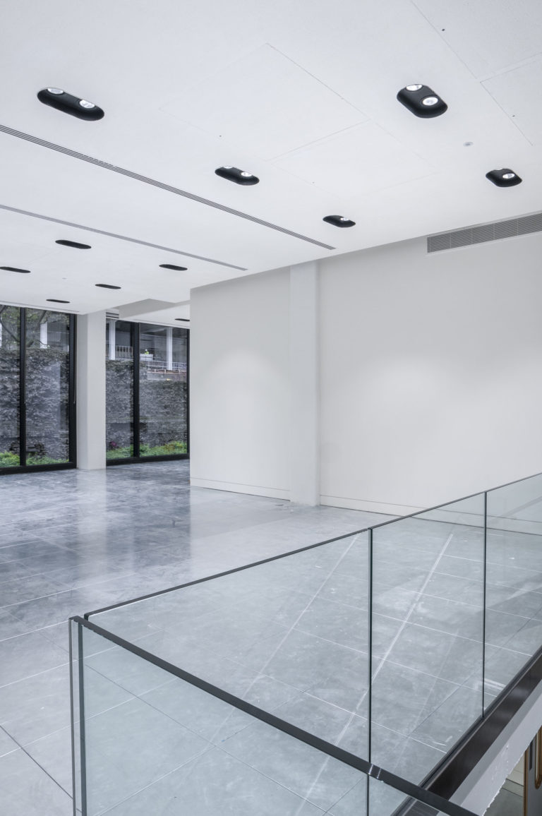 An interior of an open office space painted white with silver sub flooring. theres 2 windows on one wall and glass handrail in the forground . London Interior photographer | David Chatfield