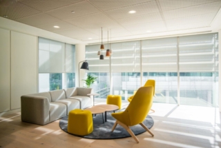 photograph of an interior of a rest room in a major company with windows in the background fitted with blinds. two orange high back chairs sat around a round table and a sofa to the left. interior photography for an office