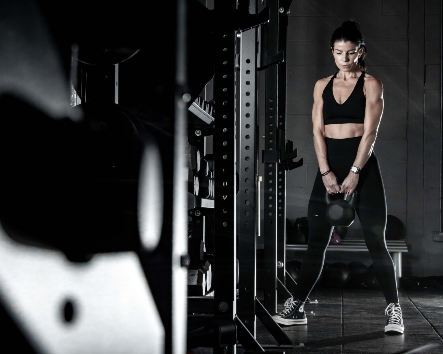 female in a gym setting working out on a machine, weaing black lycra leggings and black top, low key background. weight machines in shot