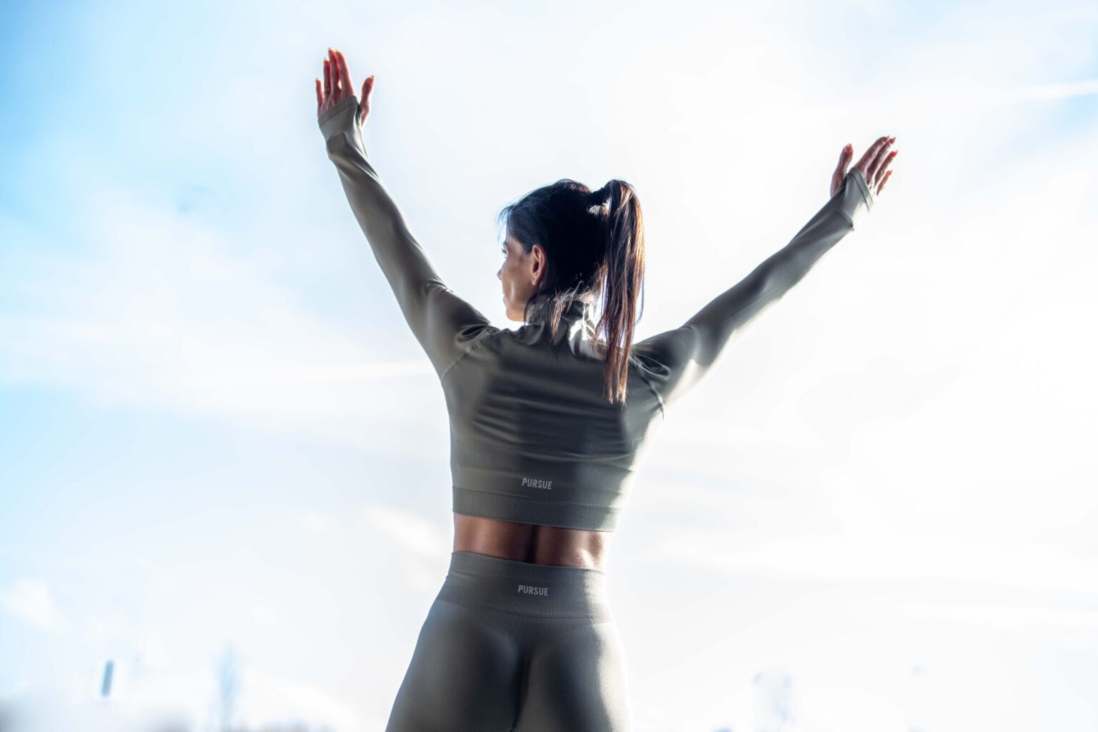 female facing the sky doing Yoga with her hands in the air, wearing green lycra gymwear