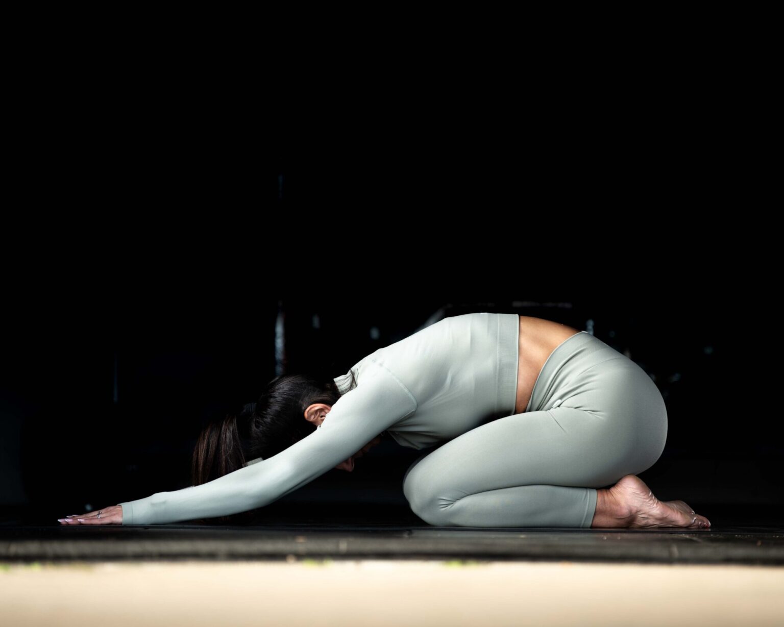 female in a gym setting doing Yoga in green lycra gymwear dark background