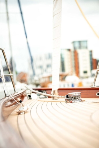 The deck of a timber yacht. in the foreground theres the yachts rigging and ropes. flats can be seen in the background.