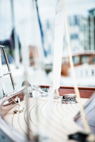 The deck of a timber yacht. in the foreground theres the yachts rigging and ropes. flats can be seen in the background.